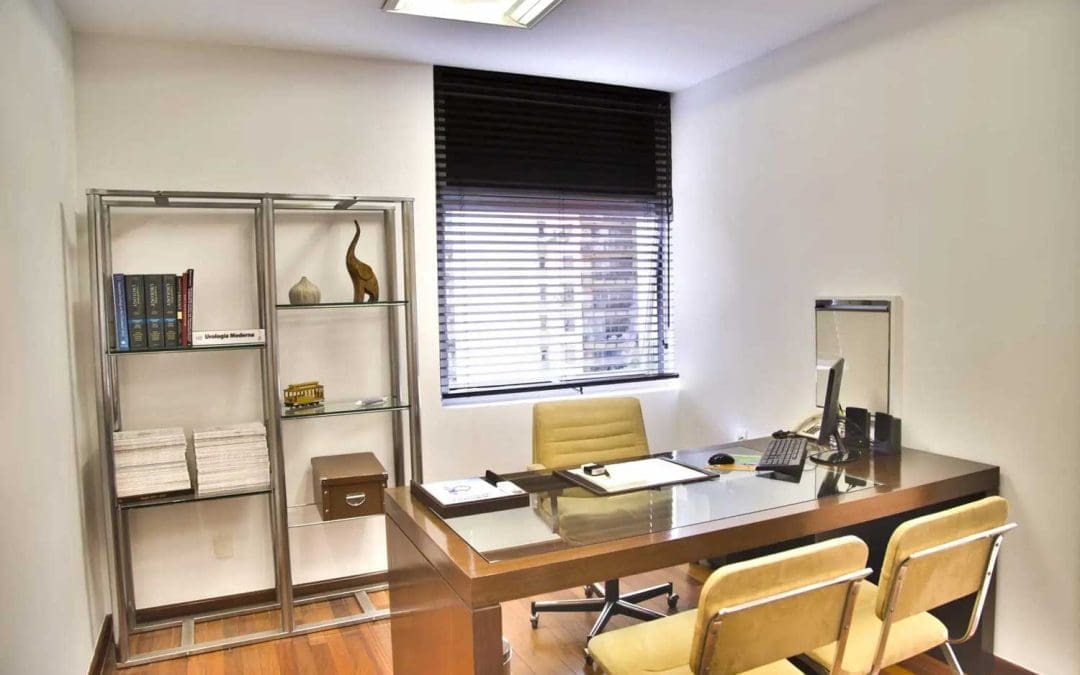 Modern office interior with glass desk, beige chairs, bookshelf, and window blinds.